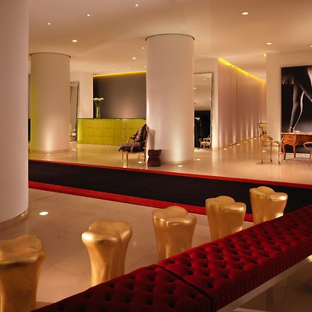 St Martins Lane London Hotel Kültér fotó The photo shows a modern and stylish interior space, possibly a lobby or a lounge area. It features sleek white pillars and a polished floor, illuminated by soft ambient lighting. On one side, there is a green seating area, while on the opposite side