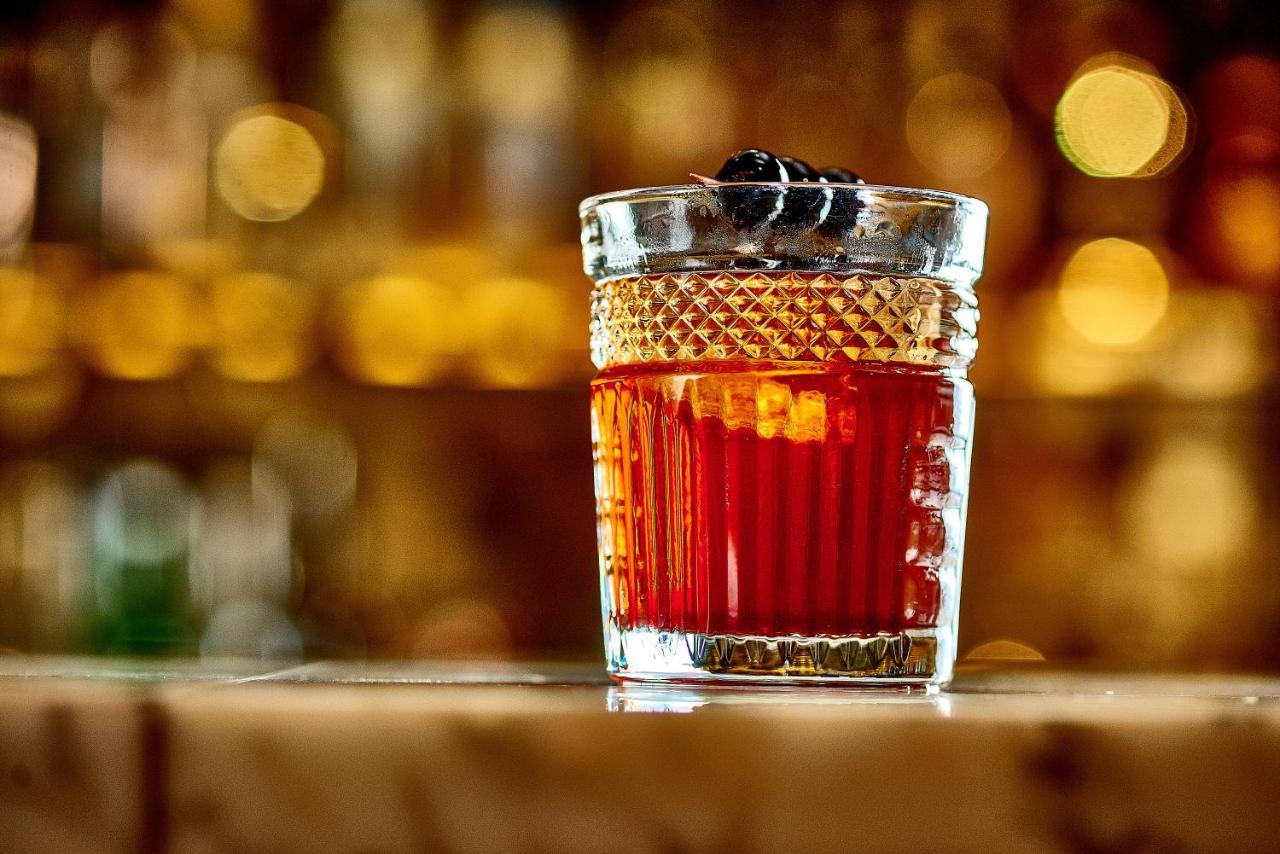 St Martins Lane London Hotel Kültér fotó The photo shows a stylish glass filled with a dark red cocktail. The glass has a textured design and is topped with a couple of dark garnishes, possibly cherries. The background is softly blurred, highlighting the drink and suggesting a warm, invitin