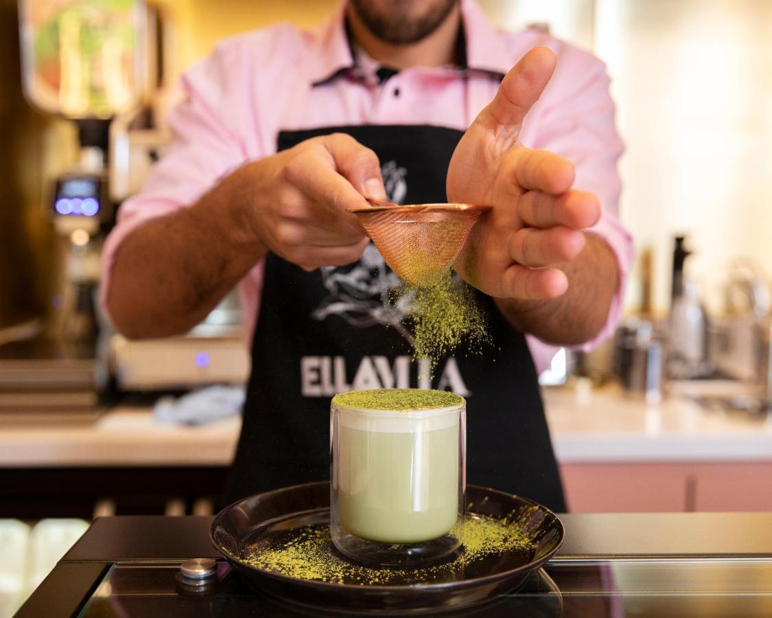 St Martins Lane London Hotel Kültér fotó The image shows a person preparing a drink, likely a matcha-based beverage. They are wearing an apron and using a small scoop to sprinkle what appears to be green matcha powder into a glass. The glass is filled with a light green drink, possibly matc