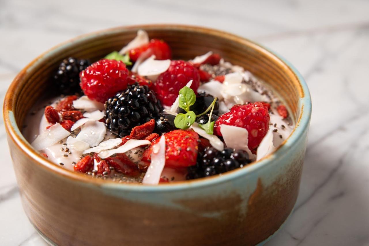 St Martins Lane London Hotel Kültér fotó The photo shows a bowl of yogurt topped with various fresh fruits and toppings. The toppings include vibrant red raspberries, blackberries, and pieces of dried fruits, along with shredded coconut. There are also some small seeds, possibly chia seeds,