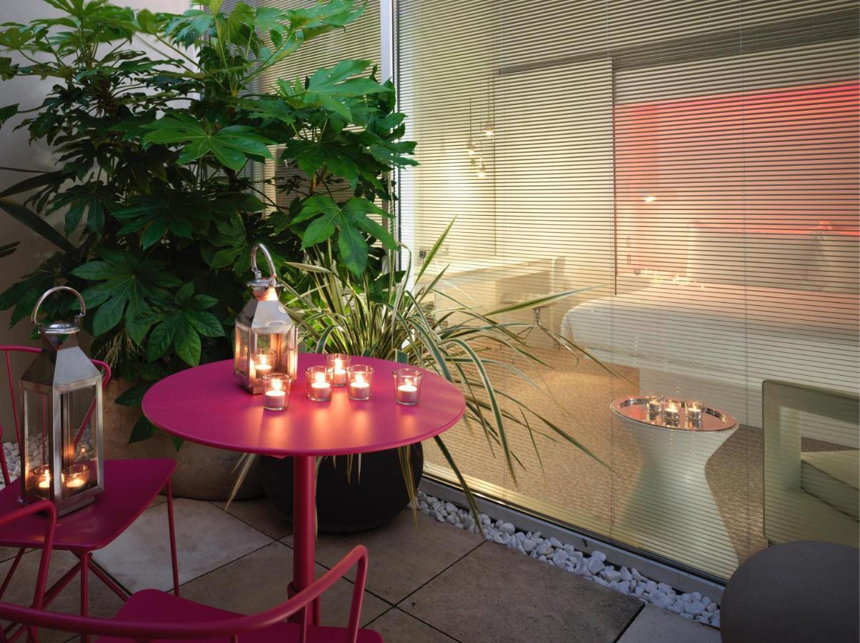 St Martins Lane London Hotel Kültér fotó The photo depicts a cozy outdoor space with a round pink table and two matching chairs. On the table, there are several lanterns with candles inside, providing a warm ambiance. Surrounding the area are lush green plants, adding a natural touch. In th