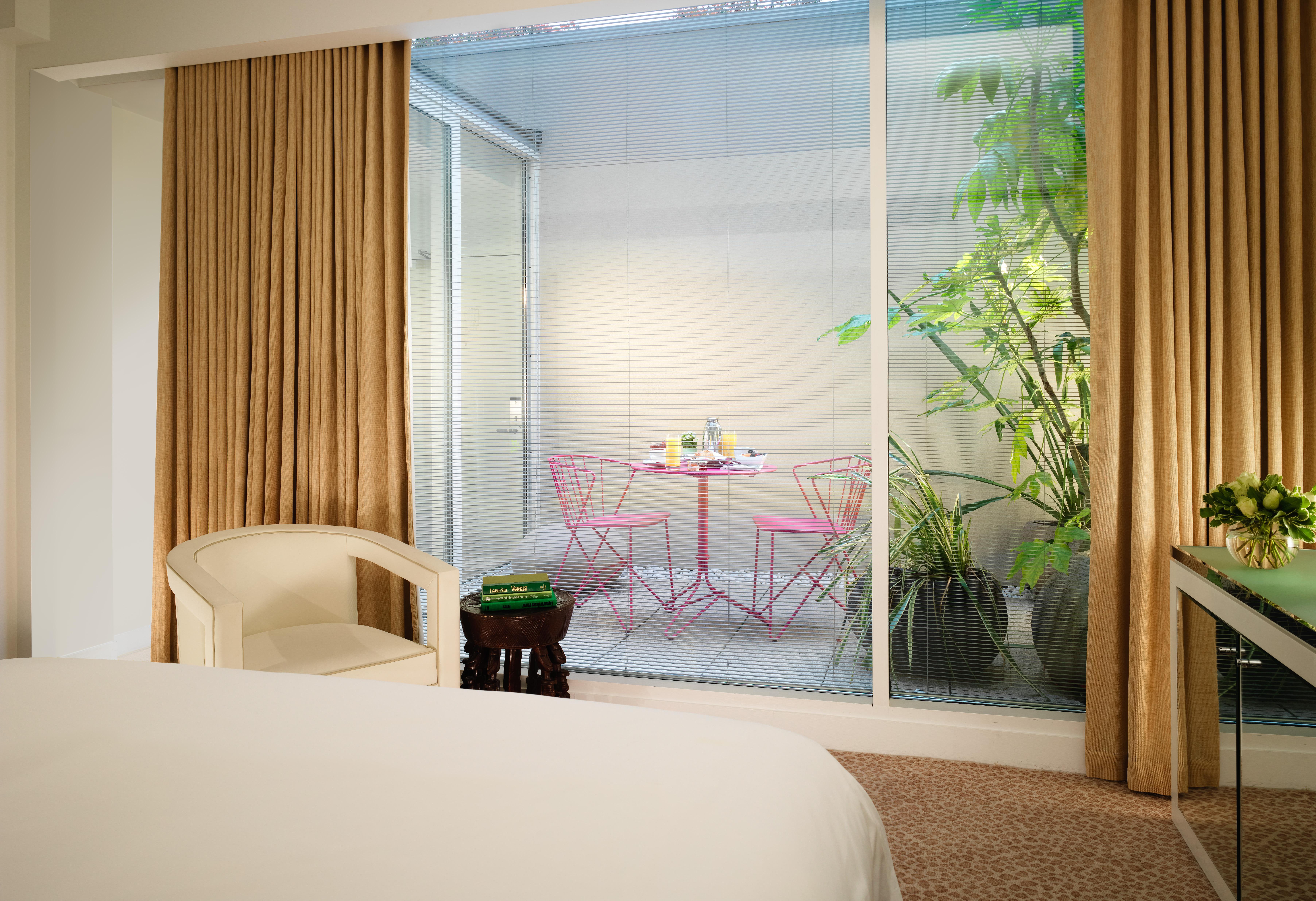 St Martins Lane London Hotel Kültér fotó The photo depicts a modern room with a bed visible in the foreground. Large glass windows allow natural light to enter, showcasing a small outdoor space. Beyond the glass, there is a charming patio area featuring a round table and two pink chairs, su