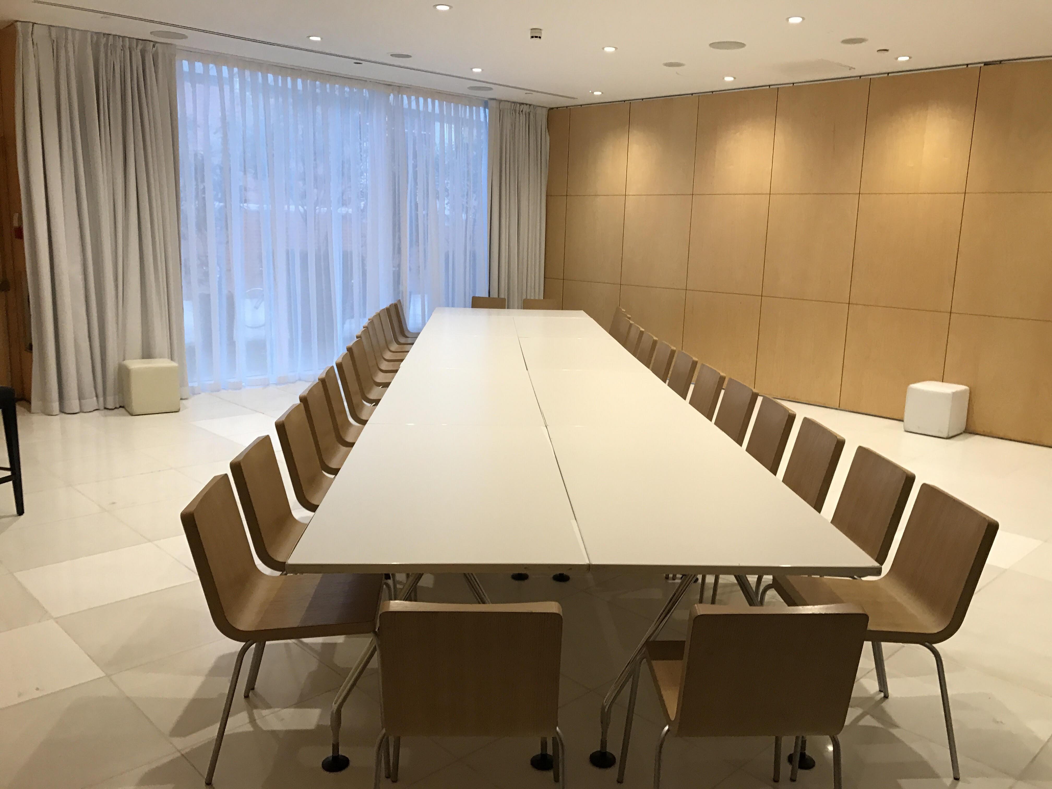 St Martins Lane London Hotel Kültér fotó The photo shows a spacious meeting room with a long, white table surrounded by wooden chairs. The room features large windows with light-colored curtains, allowing natural light to enter. The walls are made of light wood panels, creating a warm and m