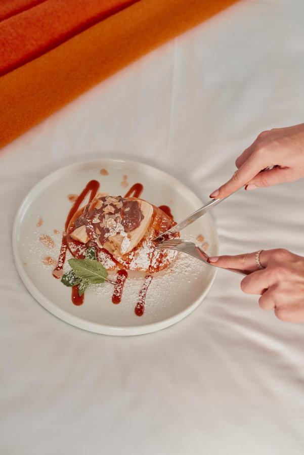 St Martins Lane London Hotel Kültér fotó The photo depicts a dessert served on a white plate. A person is using a fork and knife to cut into a piece of the dessert, which appears to be a layered cake or pastry topped with chocolate and perhaps caramel sauce. The dessert is garnished with po