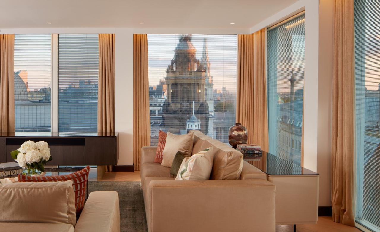 St Martins Lane London Hotel Kültér fotó The photo depicts a stylish and modern living room space. The room features large windows with sheer curtains, allowing natural light to fill the area. A plush beige sofa with decorative cushions is positioned centrally, creating a cozy atmosphere. I