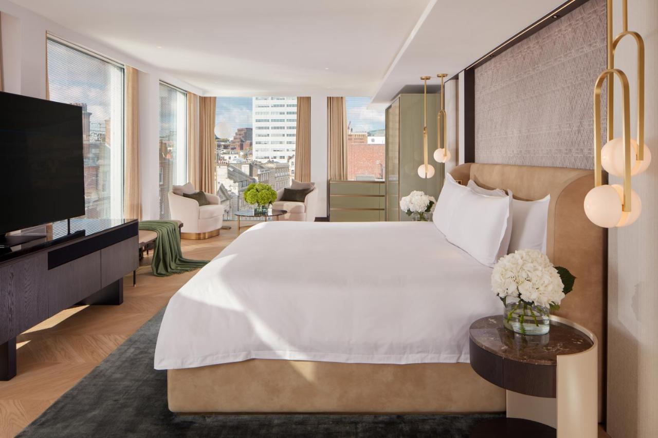 St Martins Lane London Hotel Kültér fotó The photo shows a modern hotel room featuring a large, comfortable bed with white bedding. The room has large windows that provide natural light and a view of the cityscape outside. There is a stylish flat-screen TV mounted on the wall and a dark woo