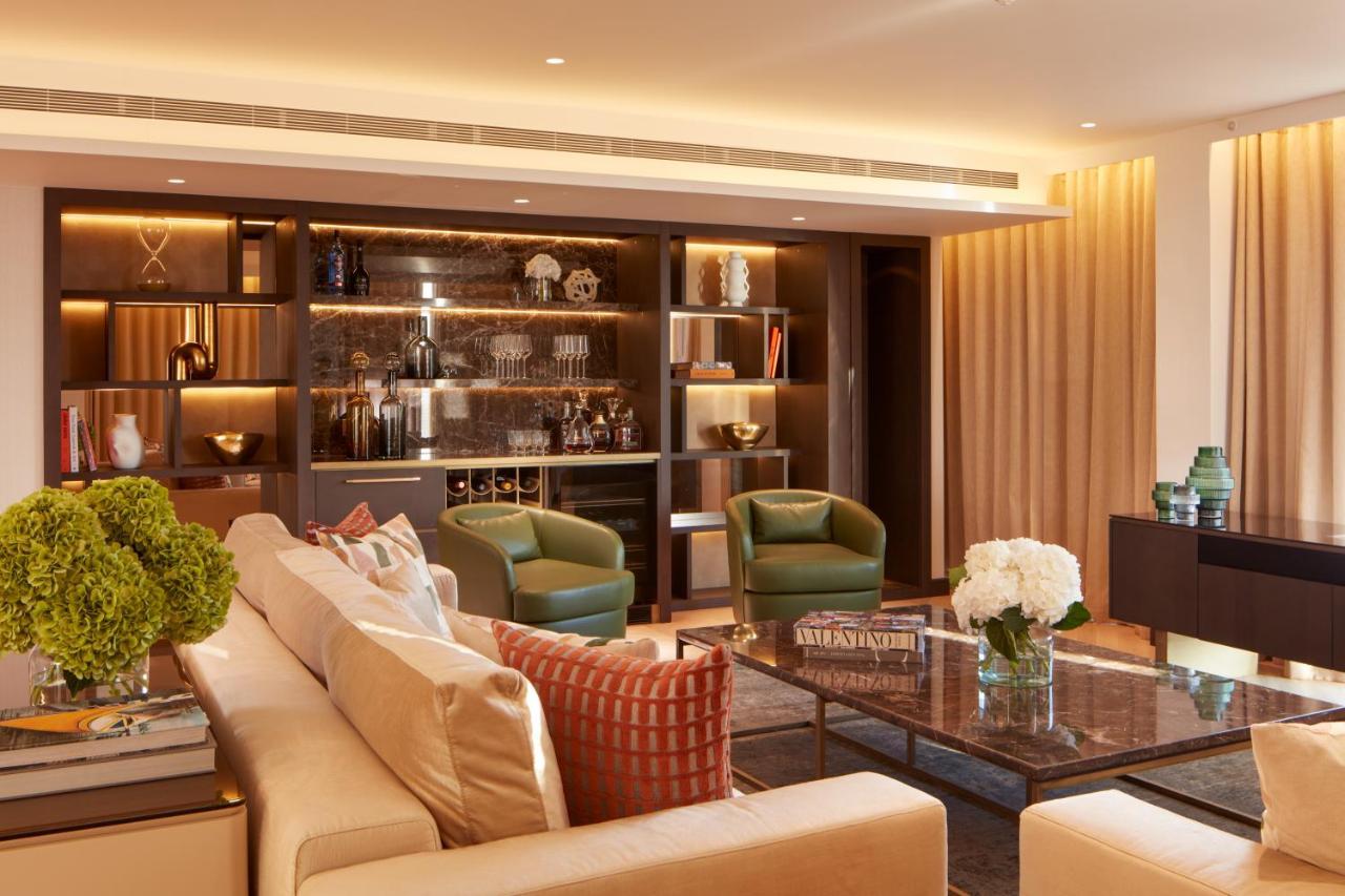 St Martins Lane London Hotel Kültér fotó The photo depicts a modern and elegantly designed living room. It features a light-colored sofa with decorative cushions, positioning it as a central seating area. Two green armchairs are placed beside a glass coffee table, which sits atop a textured