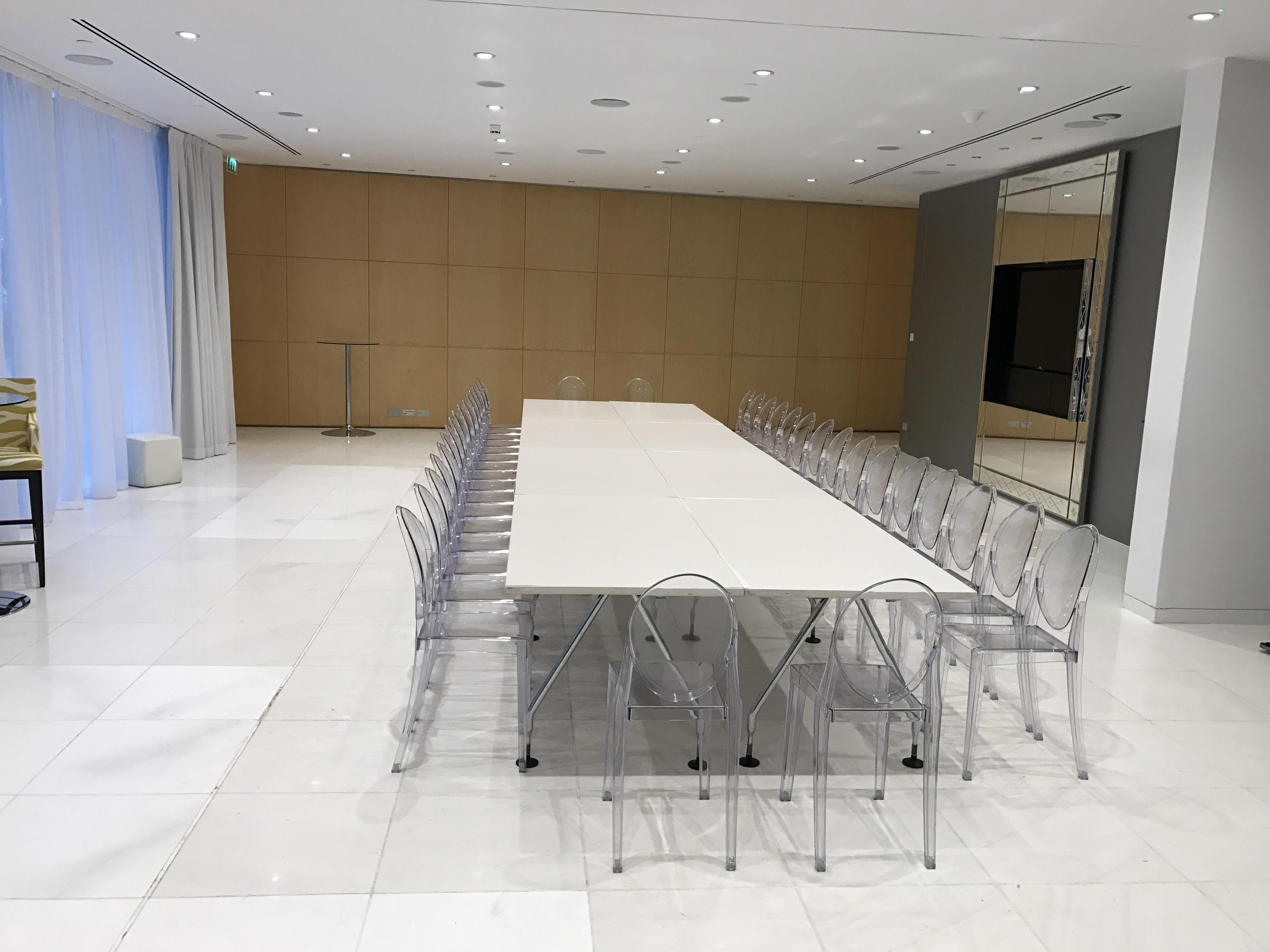 St Martins Lane London Hotel Kültér fotó The photo shows a modern meeting room or conference space. There is a long rectangular table in the center, surrounded by transparent acrylic chairs. The room features white marble flooring and appears bright due to the overhead lighting. On one side