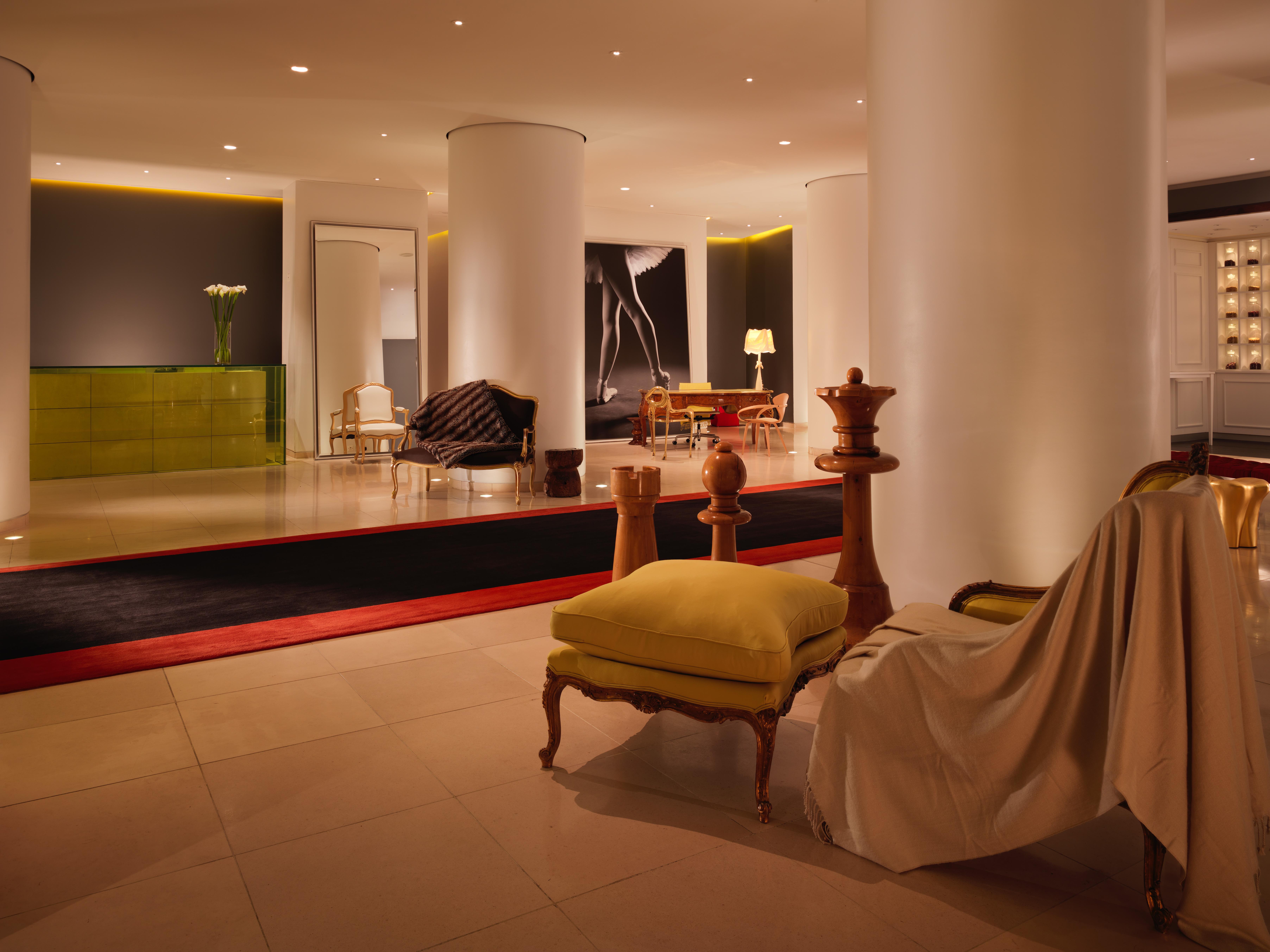 St Martins Lane London Hotel Kültér fotó The photo shows a modern, stylish hotel lobby. It features a spacious open area with sleek white columns and subtle lighting. There are various seating arrangements, including a sofa and armchairs, with a mix of contemporary and classic design elemen