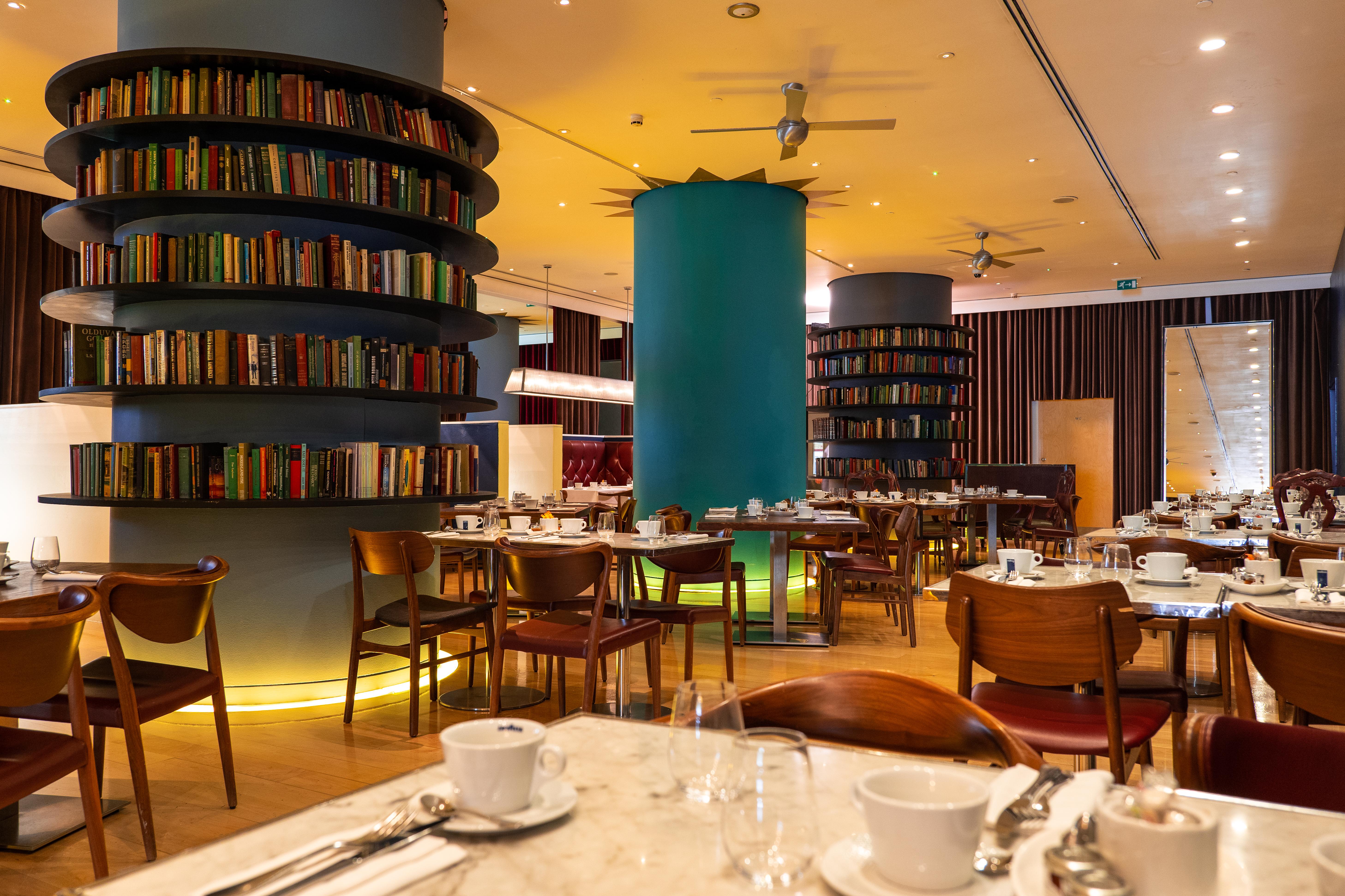 St Martins Lane London Hotel Kültér fotó The photo depicts a modern restaurant interior featuring a warm and inviting design. There are round tables set for dining, each equipped with white tableware and cutlery. The restaurant has wooden chairs and is illuminated with soft lighting. 

Nota