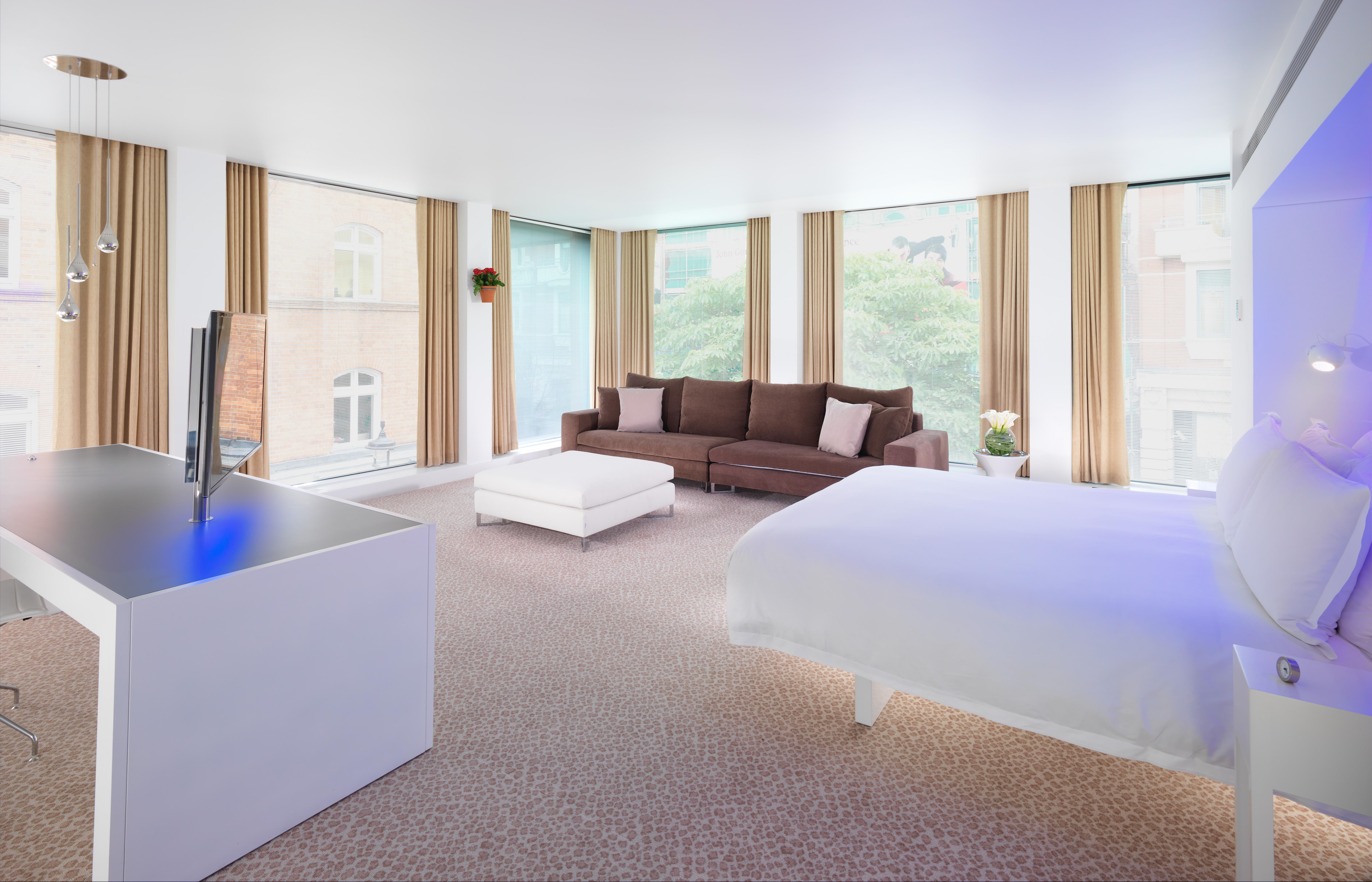 St Martins Lane London Hotel Kültér fotó The photo shows a modern hotel room with a spacious and bright interior. On one side, there is a large bed with a white comforter. To the other side, there is a cozy brown sofa with some decorative cushions. A white coffee table is placed in front of
