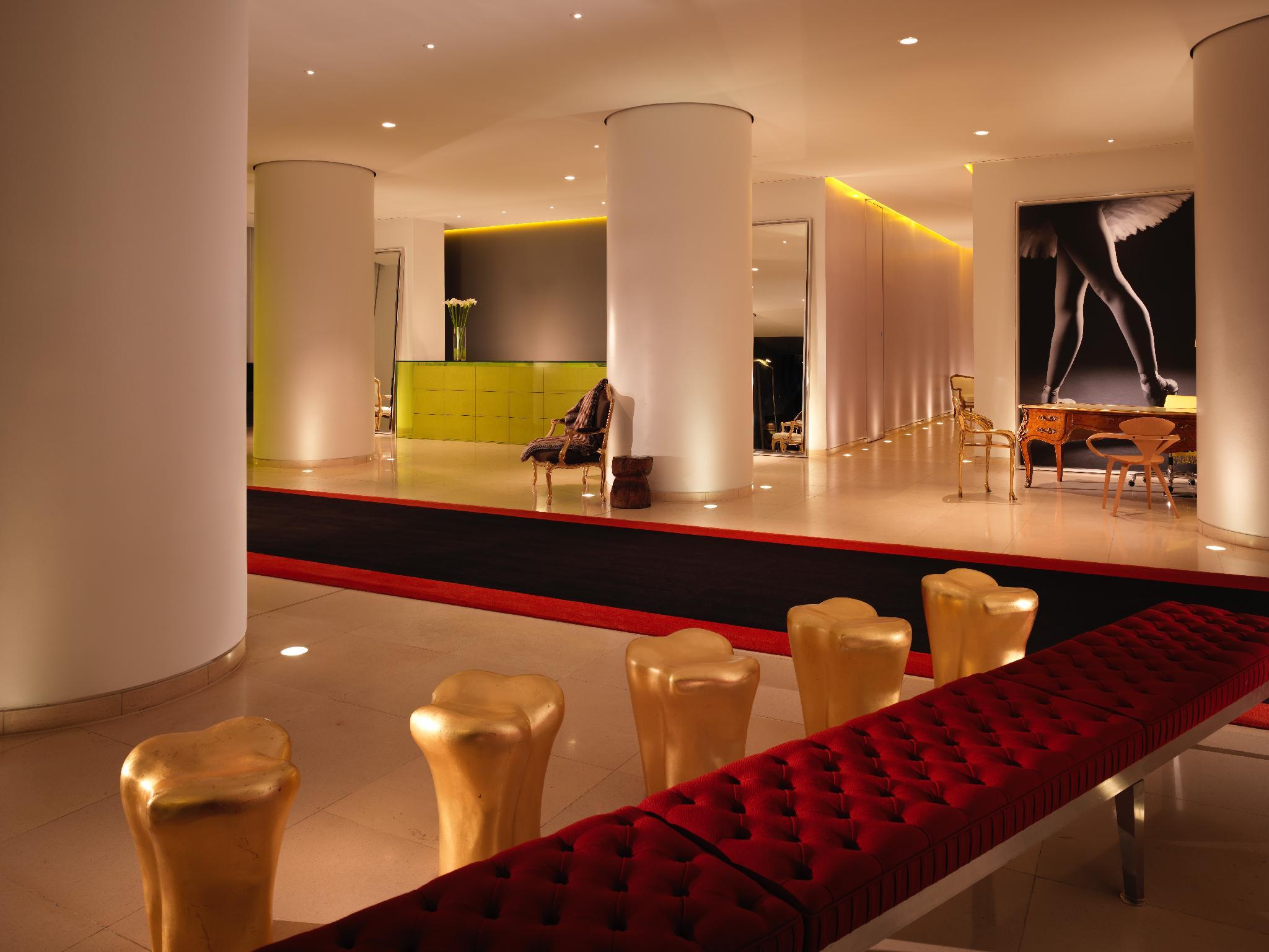 St Martins Lane London Hotel Kültér fotó The photo shows a modern and stylish interior space, possibly a lobby or a lounge area. It features sleek white pillars and a polished floor, illuminated by soft ambient lighting. On one side, there is a green seating area, while on the opposite side