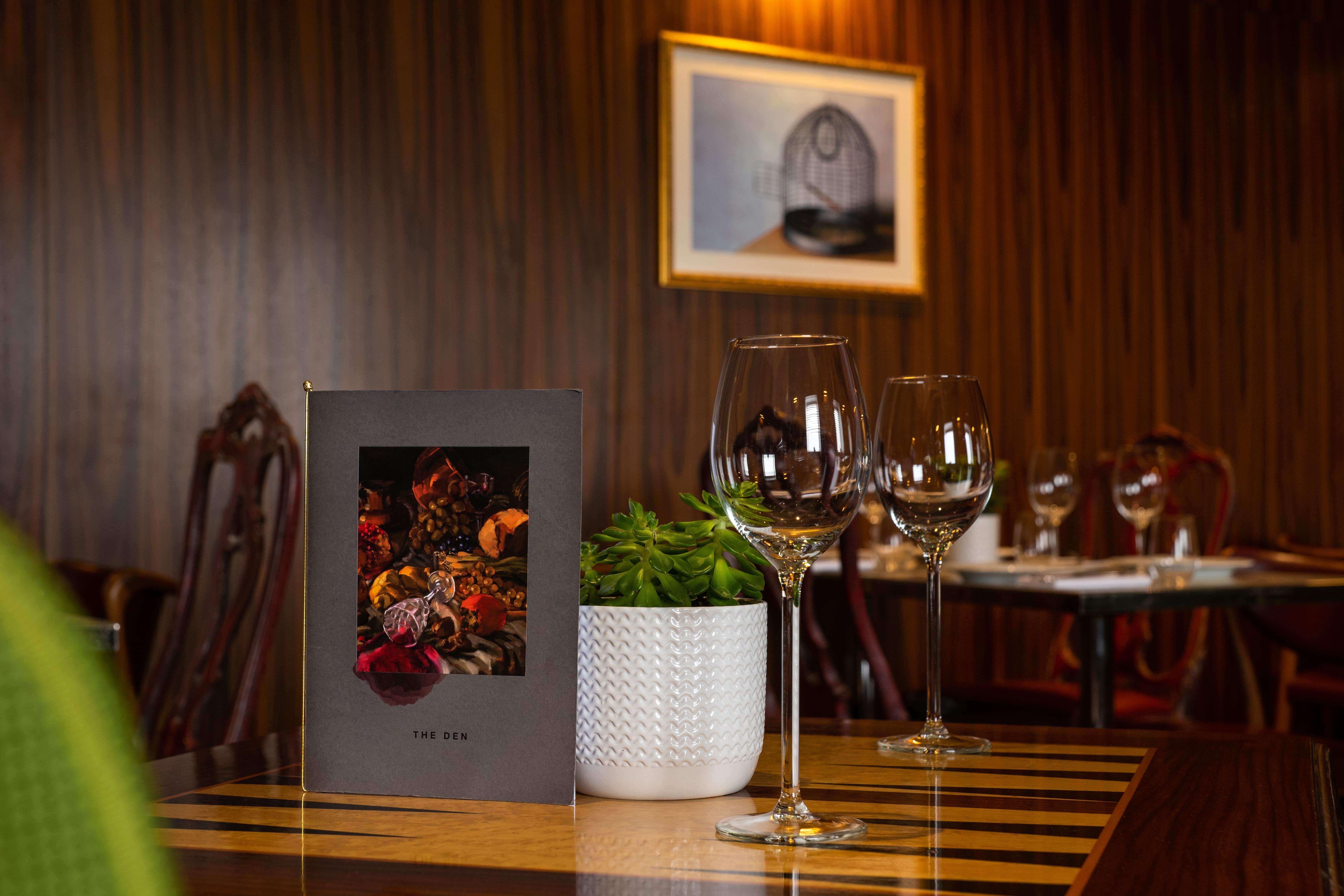 St Martins Lane London Hotel Kültér fotó The photo shows a cozy dining setting in a restaurant. A menu is prominently displayed on the table, featuring a colorful design that includes images of spices or garnishes. Next to the menu, there are two elegant wine glasses, reflecting the ambianc