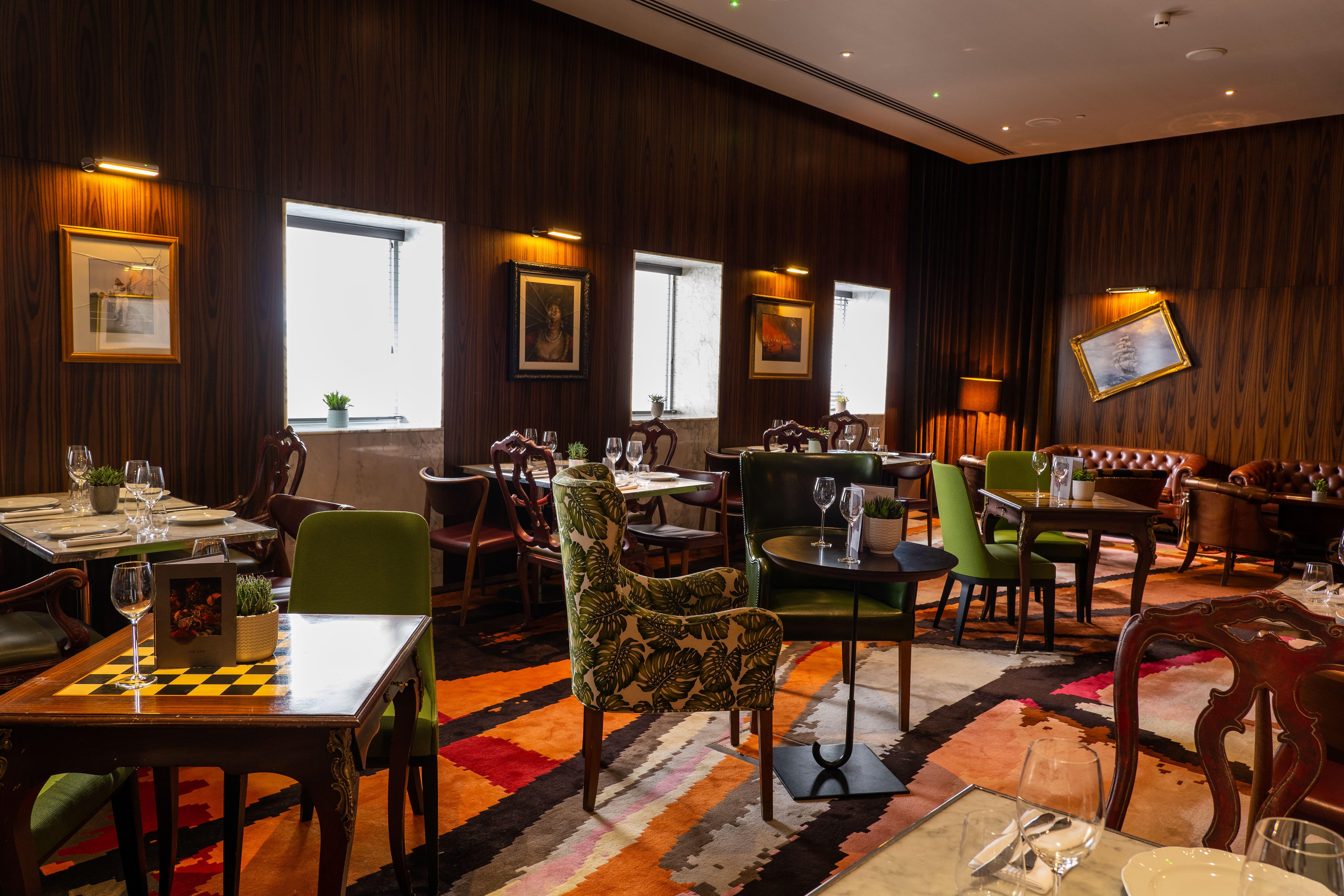 St Martins Lane London Hotel Kültér fotó The photo depicts an elegantly designed restaurant interior. It features a combination of wooden walls and warm lighting, creating a cozy atmosphere. The seating comprises various styles of chairs, some with colorful upholstery and patterns. Tables a