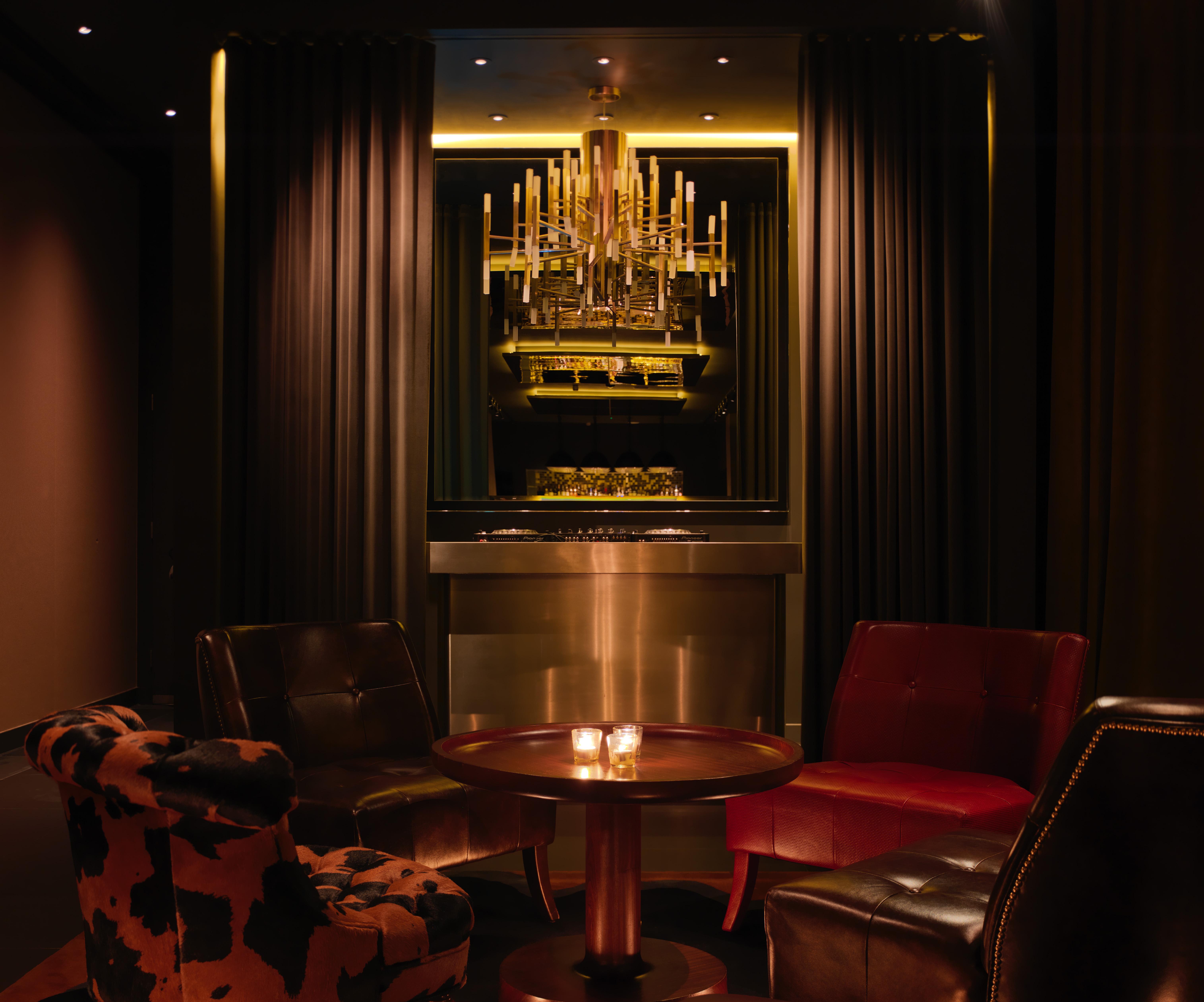 St Martins Lane London Hotel Kültér fotó The photo depicts a stylish and elegant lounge area. There are two armchairs, one in a deep red and another upholstered in a cowhide pattern. A round table is situated in the center, with two lit candles adding a warm ambiance. In the background, the