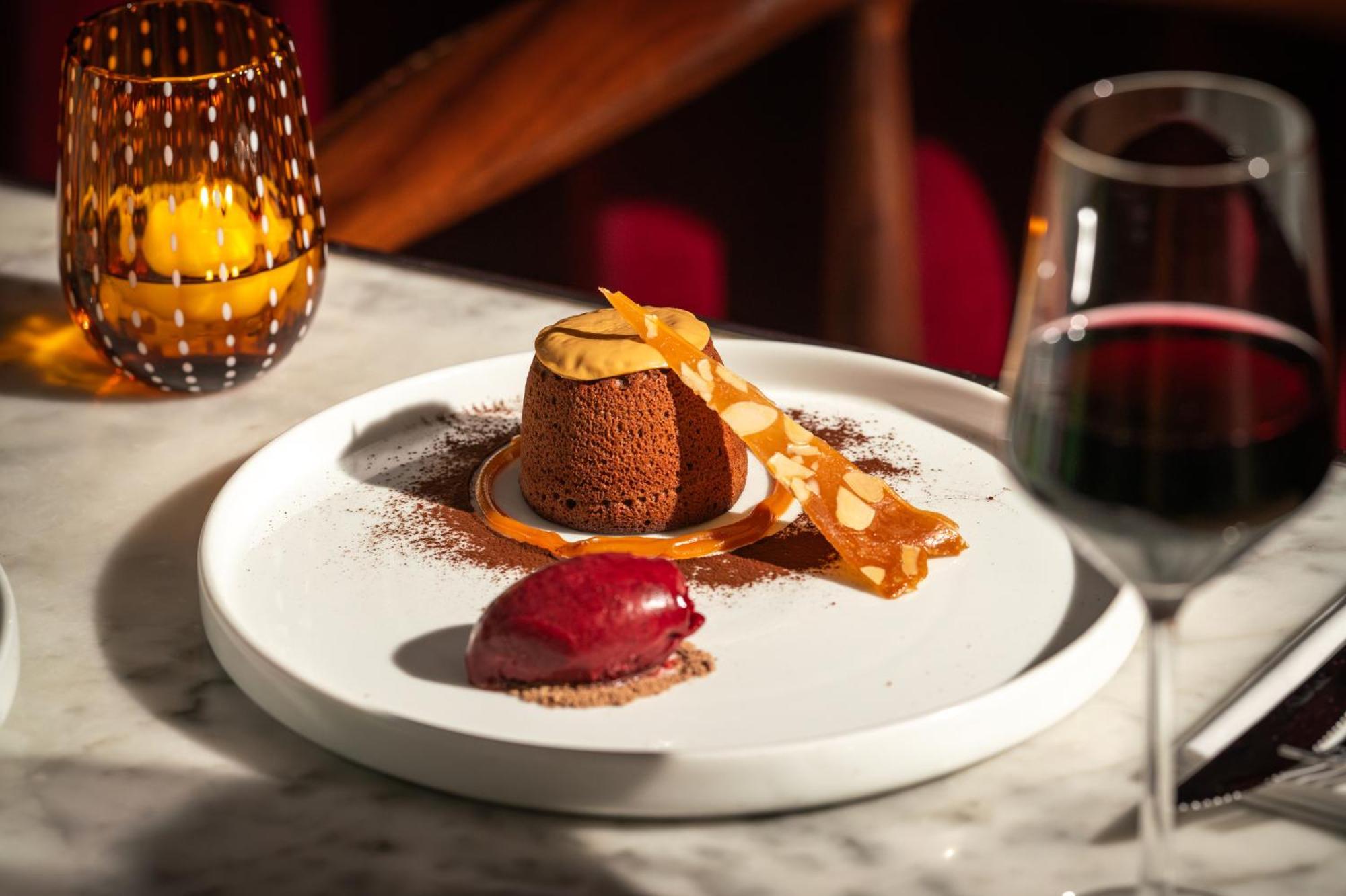 St Martins Lane London Hotel Kültér fotó The photo showcases an elegantly presented dessert on a white plate. At the center is a chocolate dessert, likely a mousse or soufflé, adorned with a delicate strip of caramel or chocolate. Surrounding it is a sprinkle of cocoa powder. Beside the cho