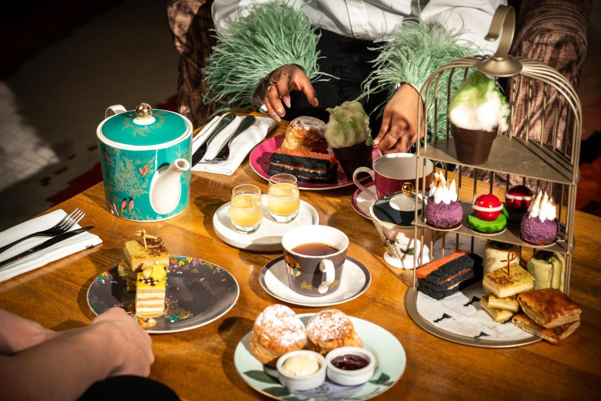 St Martins Lane London Hotel Kültér fotó The photo features a beautifully arranged afternoon tea setting. In the center, there's an elegant tiered stand filled with various desserts, including colorful cupcakes and small pastries. Surrounding the stand are plates with additional treats, suc