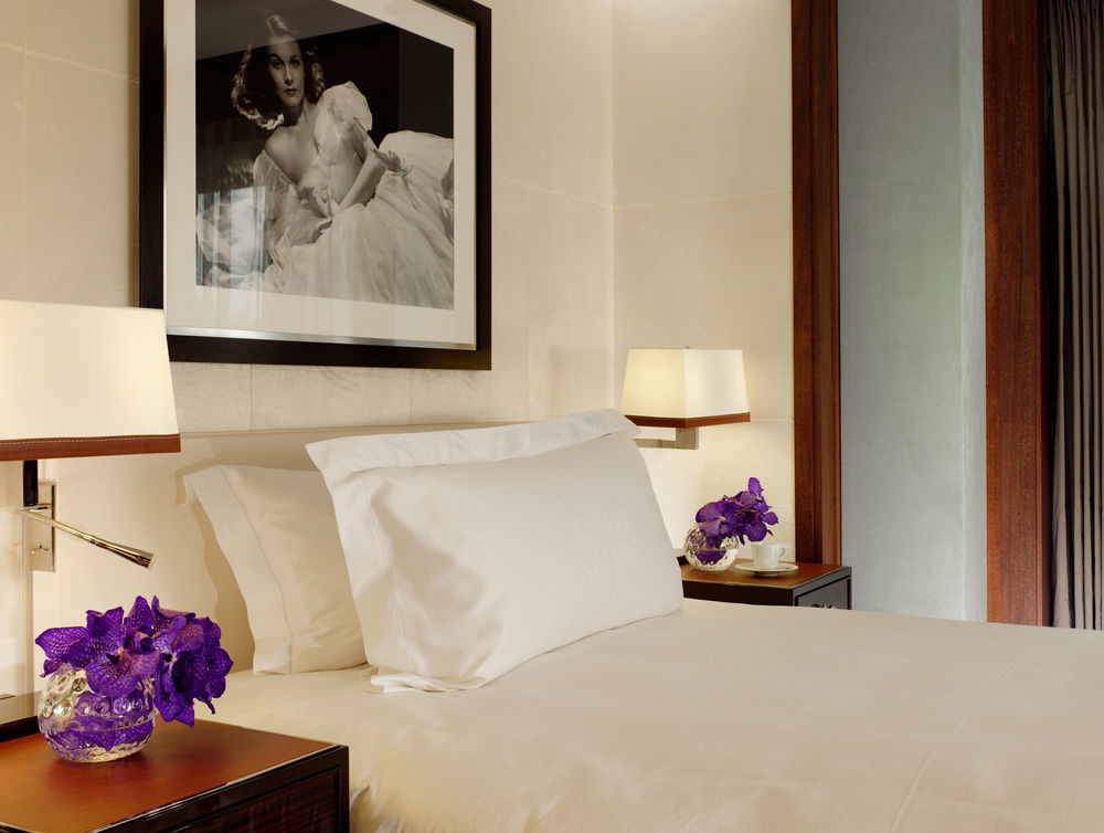 St Martins Lane London Hotel Kültér fotó The photo shows a stylishly decorated bedroom. It features a neatly made bed with a white bedspread and a large white pillow. On either side of the bed, there are dark wood nightstands with decorative lamps. Each nightstand has a small vase containin