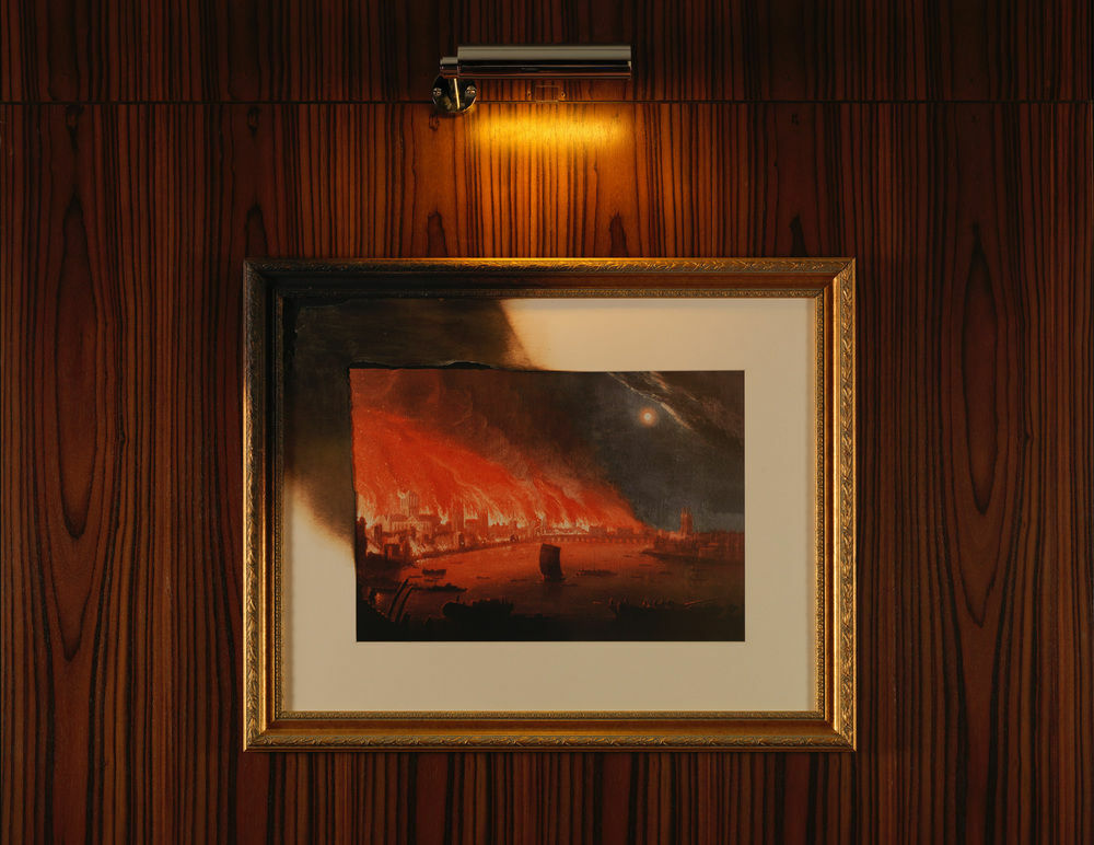St Martins Lane London Hotel Kültér fotó The photo shows a framed painting illuminated by a small light above it. The artwork depicts a dramatic scene with fiery red and orange hues, suggesting a sense of destruction or chaos. The painting is set against a wall with a wood grain texture, an