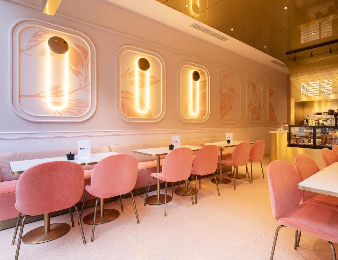 St Martins Lane London Hotel Kültér fotó The photo depicts a stylish cafe or restaurant interior. The walls are adorned with soft pastel colors, particularly muted pink tones, and feature elegant, abstract designs. There are modern pendant lights mounted on the walls, which provide warm lig